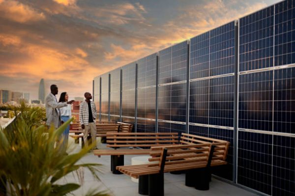 Real estate agent and couple standing on rooftop of environmentally aware office building with dramatic sky and Barcelona cityscape in background at sunset.